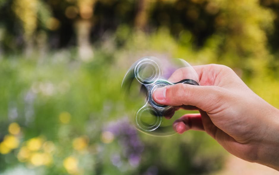 Close-up of a hand spinning a fidget spinner outdoors with a blurred natural background.
