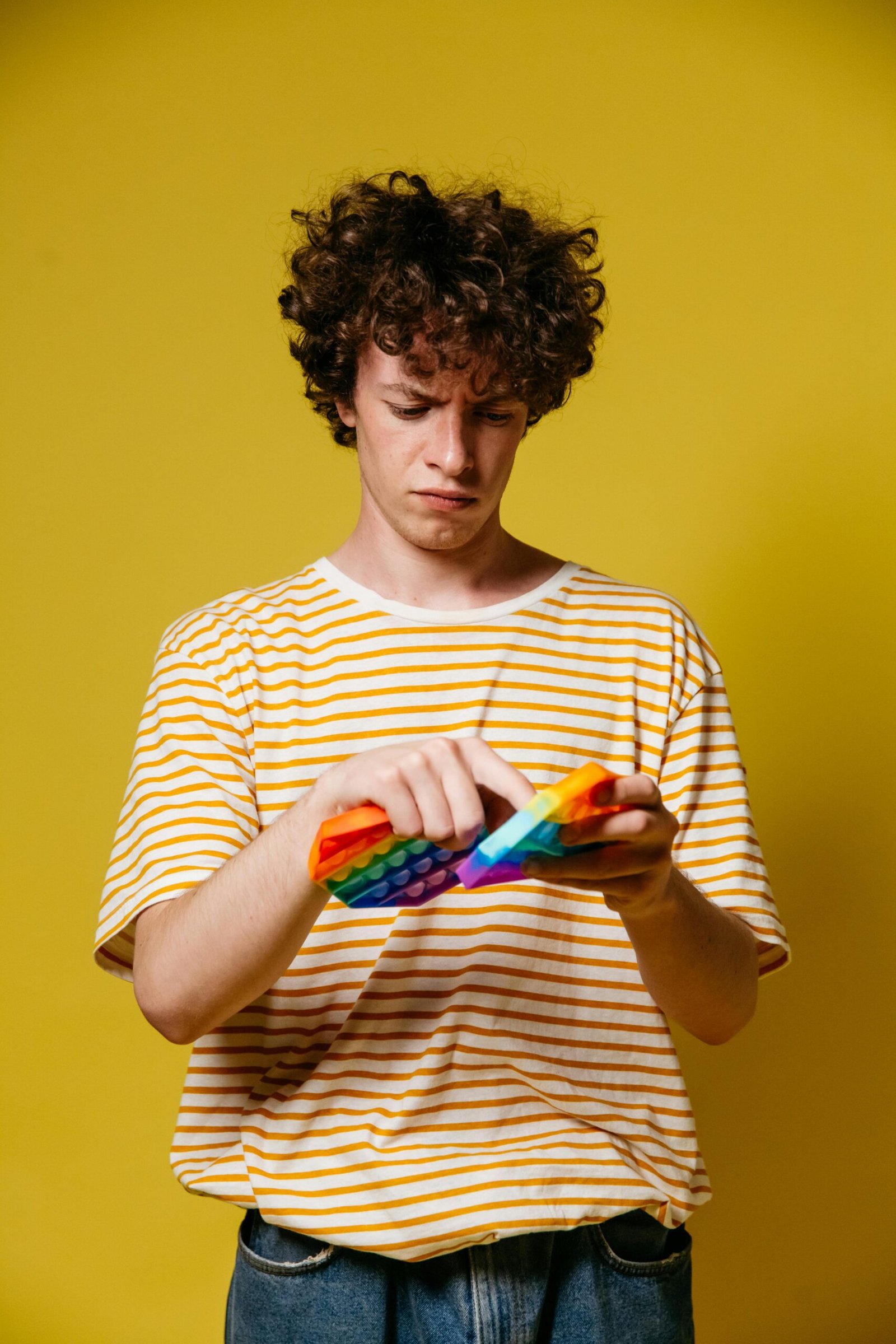 Man playing with colorful fidget toy on vibrant yellow background.